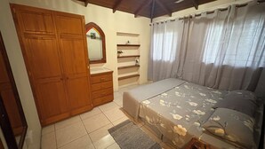 A bedroom with a bed, a wardrobe, a mirror, a shelf, and a ceiling fan.