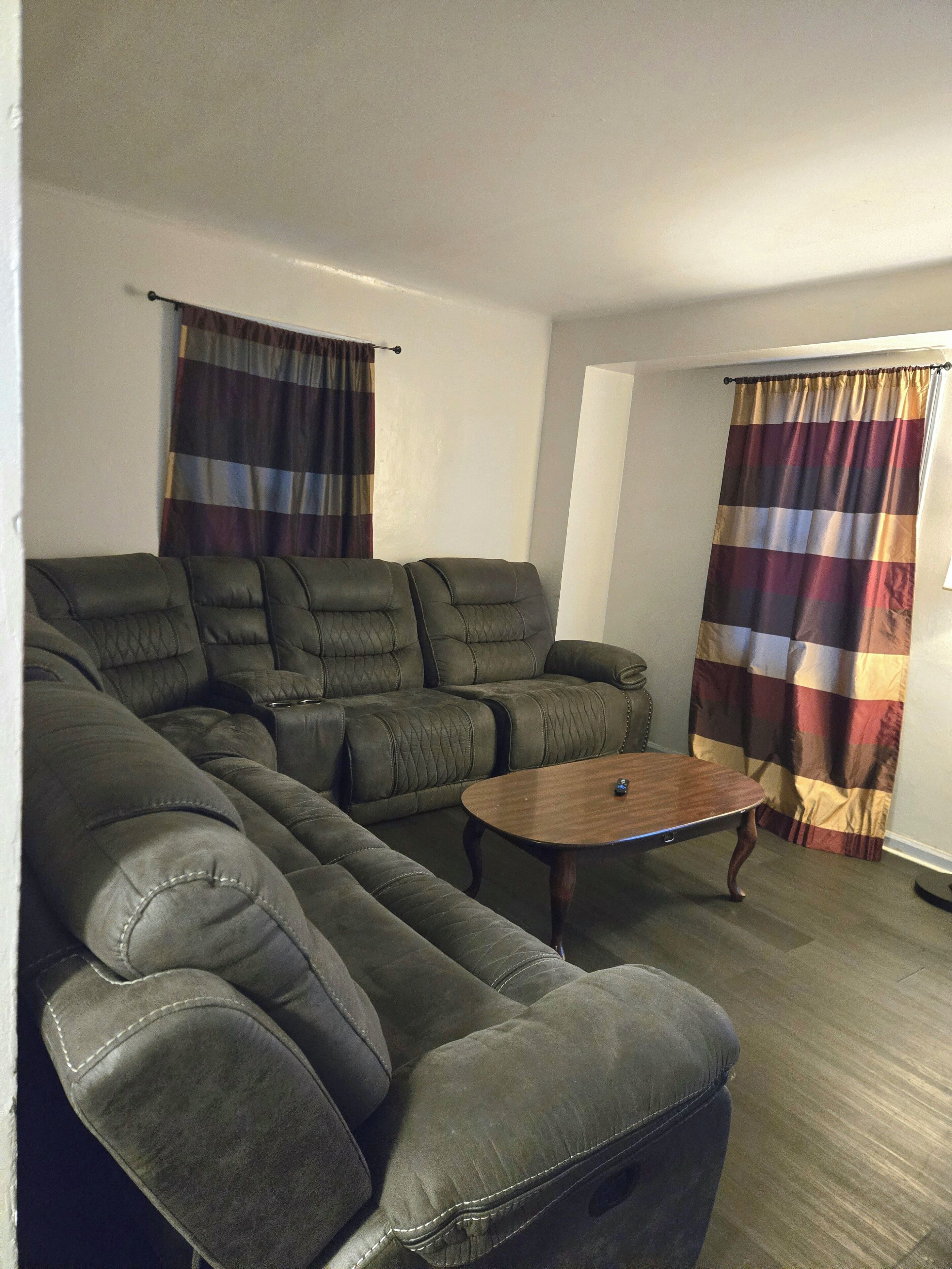 A living room with a sectional sofa, a wooden coffee table, and curtains.