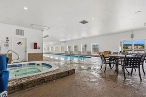 An indoor swimming pool with a hot tub, a dining area with tables and chairs, and a view of the outdoors.