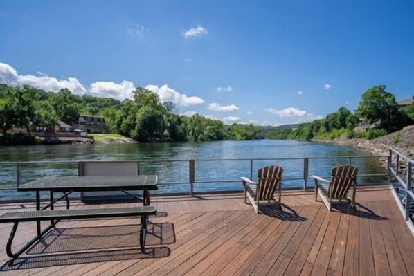 Una terraza de madera con una mesa de picnic y dos sillas Adirondack con vistas a un río.