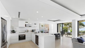 Une cuisine moderne avec des meubles blancs, un îlot central et un coin repas offrant une vue sur l’extérieur.