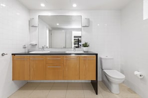 A modern bathroom with two sinks, a toilet, and a mirror above the sinks. - Apartment 03 Noosa Court  (Noosa Heads)