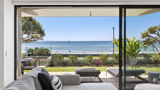 Un salon moderne doté d’une grande porte-fenêtre coulissante donnant sur un balcon avec vue sur la mer et la plage.
