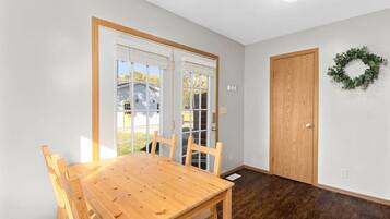 Un comedor con mesa y sillas de madera, una puerta y una guirnalda en la pared.