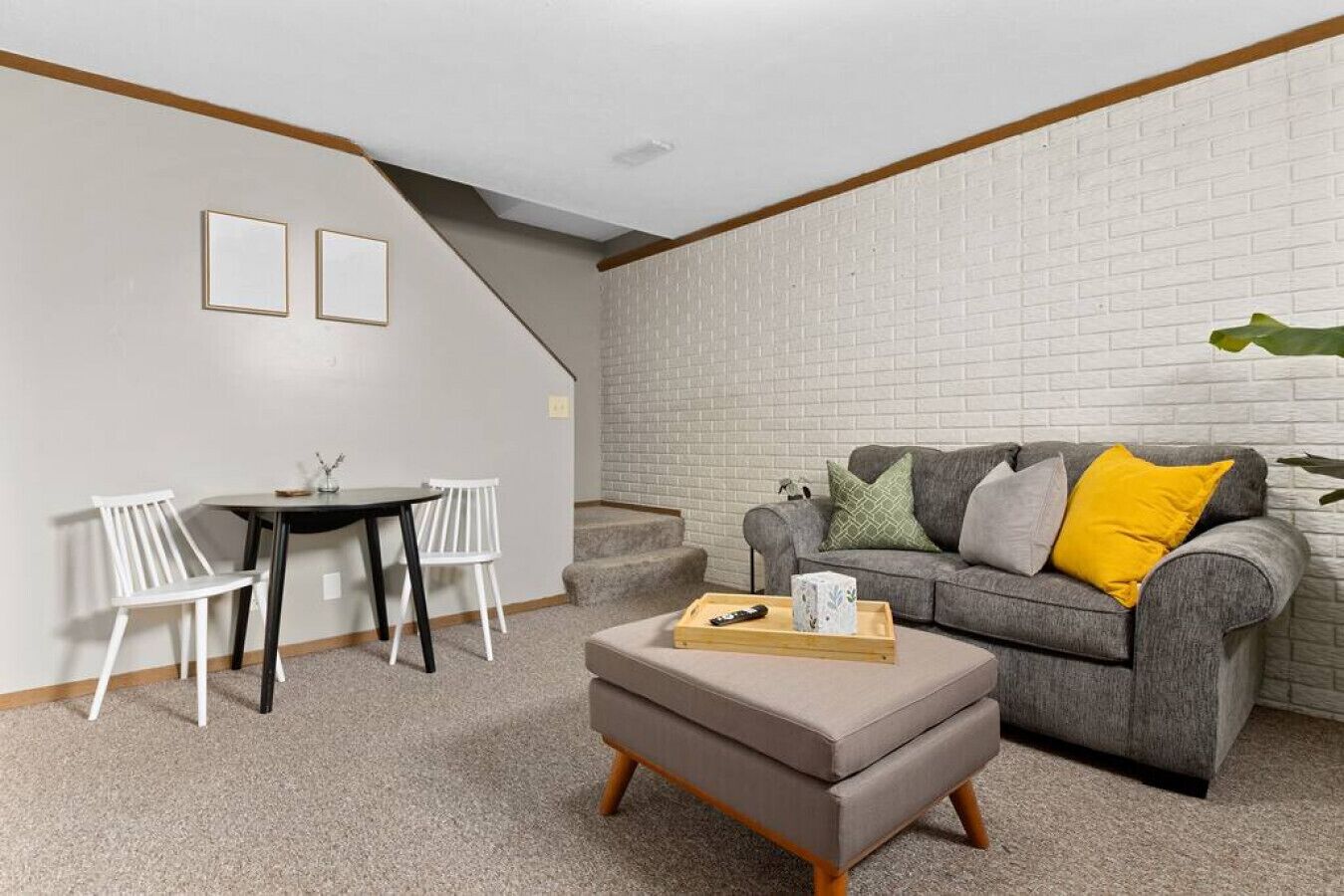 Een gezellige woonkamer met een grijze bank, een klein rond tafeltje en twee witte stoelen.