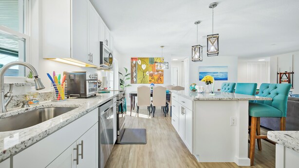 Una cocina moderna con armarios blancos, encimera de granito y comedor con sillas color turquesa.