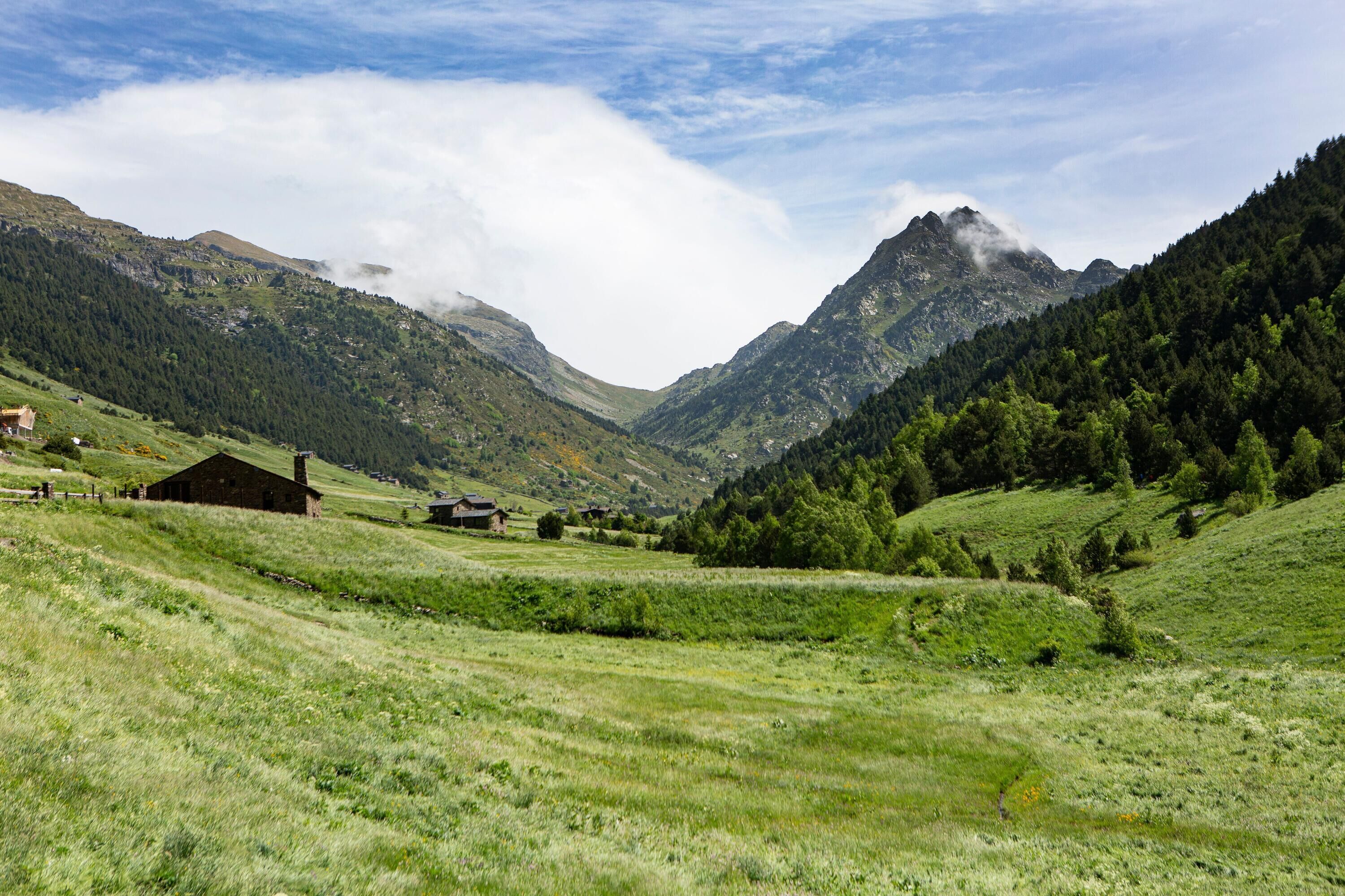 Un paysage montagneux avec une vallée, quelques bâtiments et un ciel dégagé.
