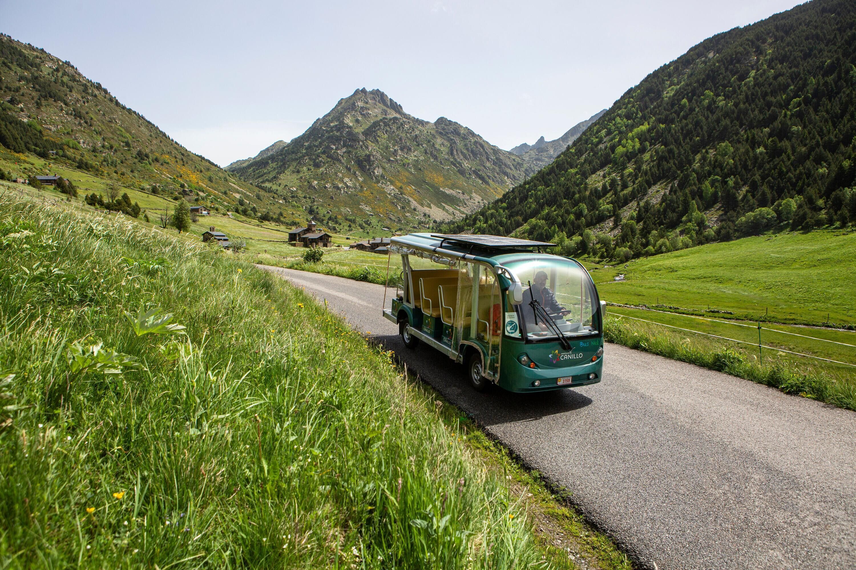 Una autocaravana verde estacionada en un camino rural con montañas al fondo.