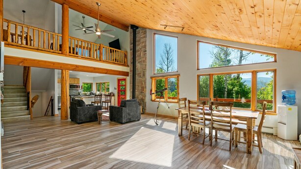A spacious living area with a wooden ceiling, large windows, a balcony, and a dining area. - Secluded Getaway Near Purgatory - Luxurious Hot Tub, Idylic 360° Views, Pets OK! (Durango)