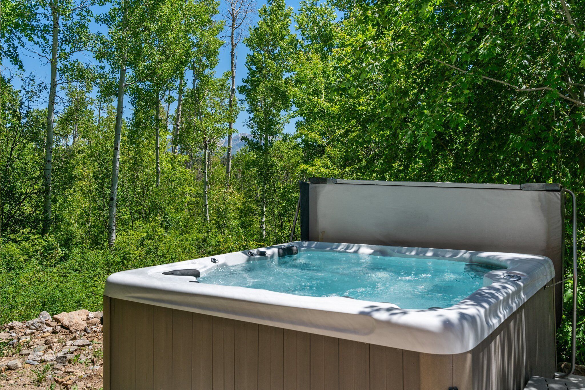 A hot tub in a forested area with a clear view of the surrounding trees and sky.