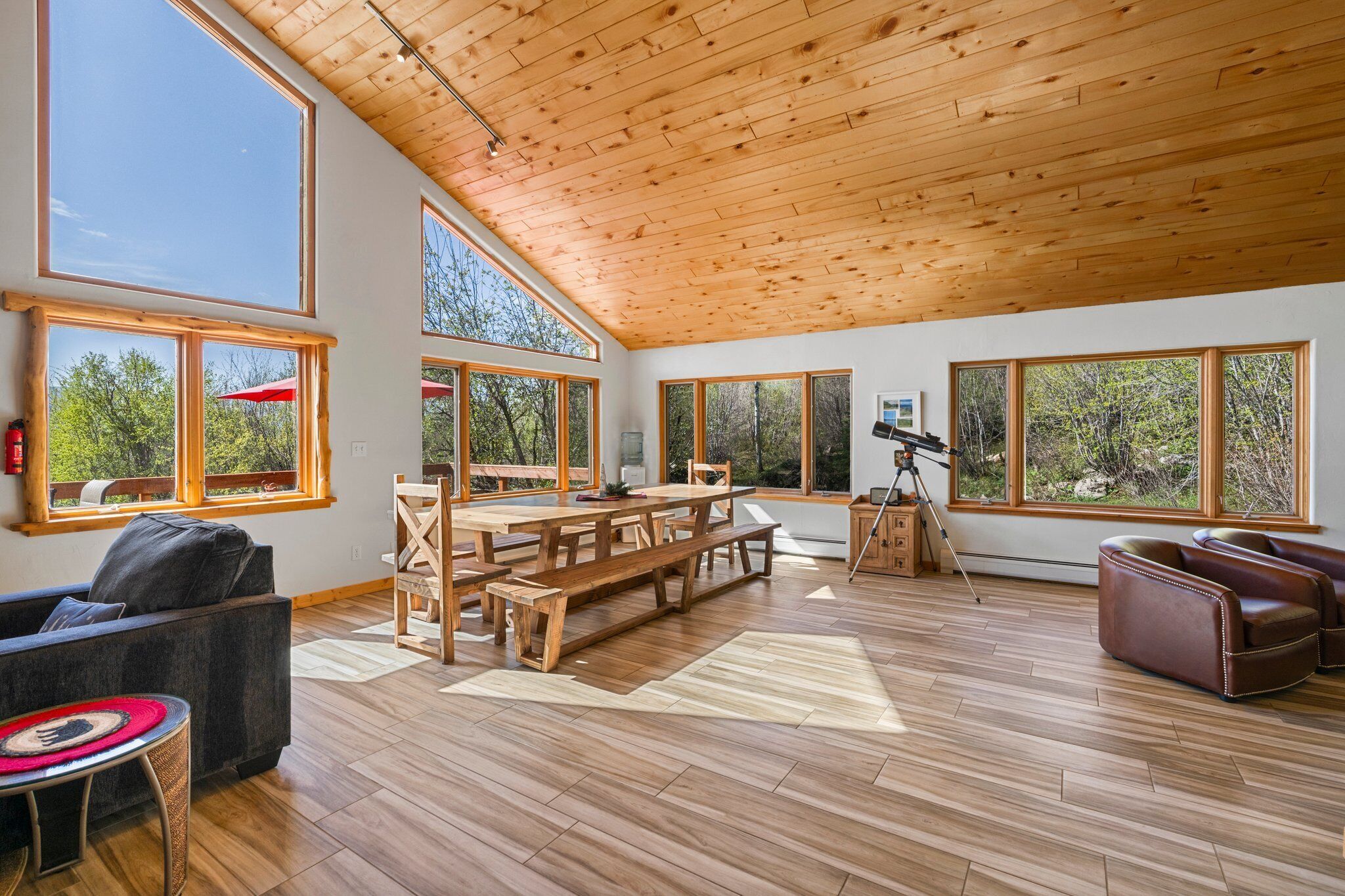 A spacious room with large windows, a wooden ceiling, and a wooden dining table.