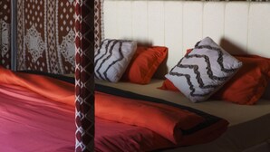 A bed with red bedding and patterned pillows, a curtain, and a patterned wall.