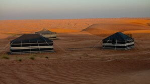 Yurts in a desert landscape with sand dunes in the background.