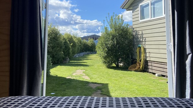 Habitació amb llit, finestra i vista cap a un jardí i una casa.