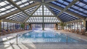 An indoor swimming pool with a glass ceiling, lounge chairs, and a view of the outside.