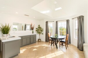 Cocina luminosa con comedor, una isla central, armarios grises y una planta en maceta.