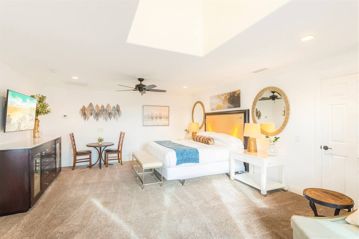 A bedroom with a bed, bedside tables, a desk, a chair, a ceiling fan, and a door.