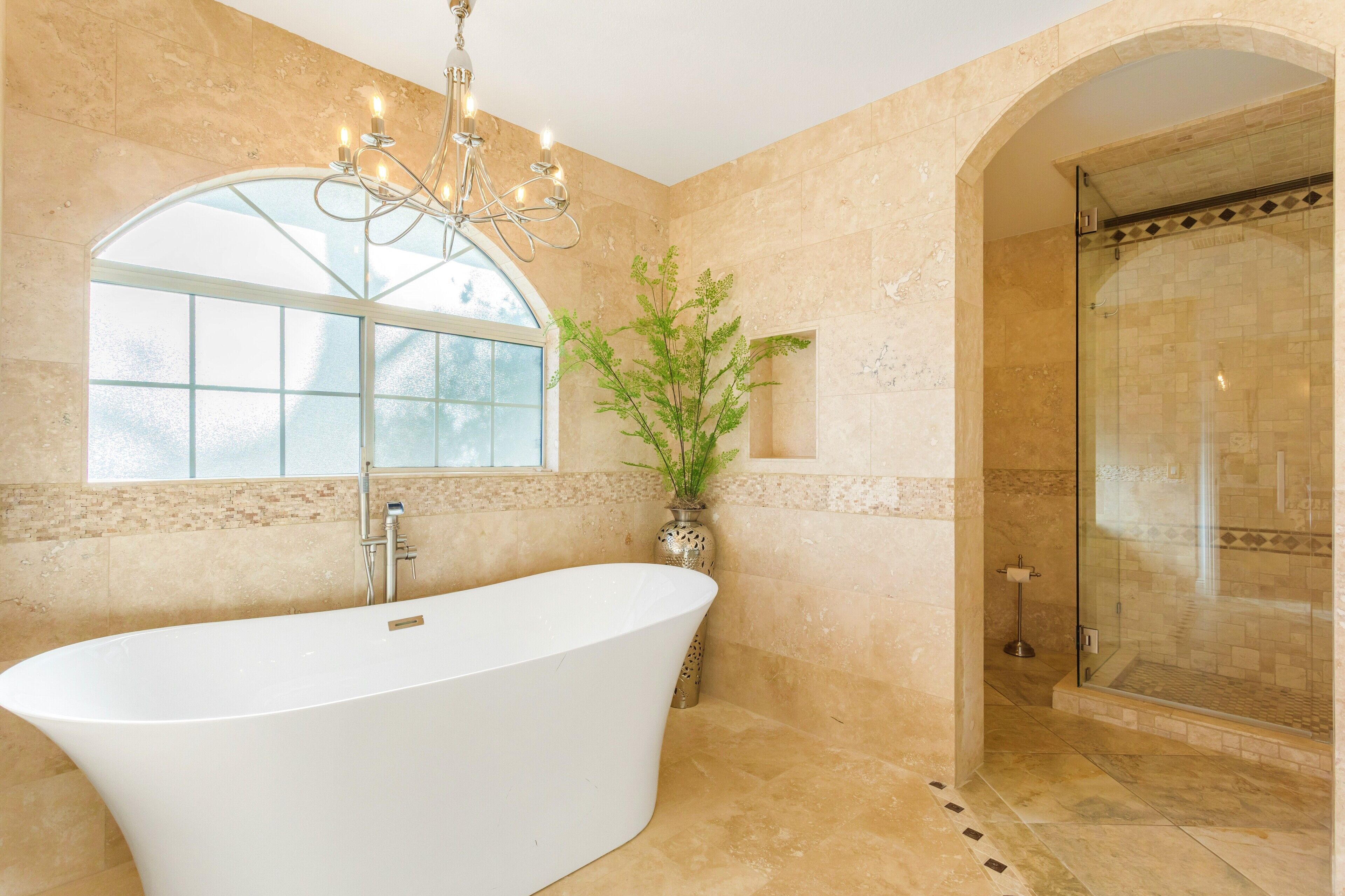 A bathroom with a freestanding bathtub, a glass shower enclosure, and a large arched window.