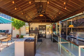An outdoor kitchen area with a grill, seating, and a refrigerator.