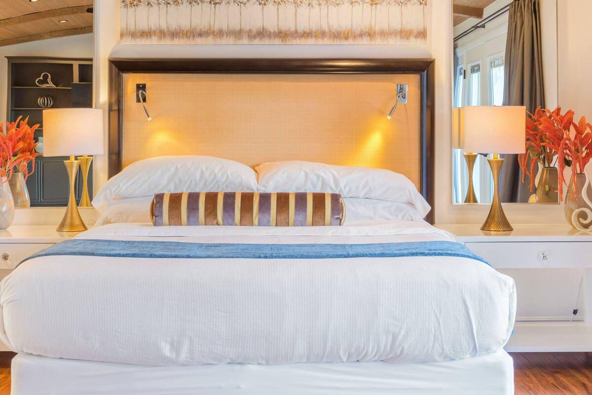 A hotel room with a large bed, two bedside tables with lamps, a dresser, and a mirror.