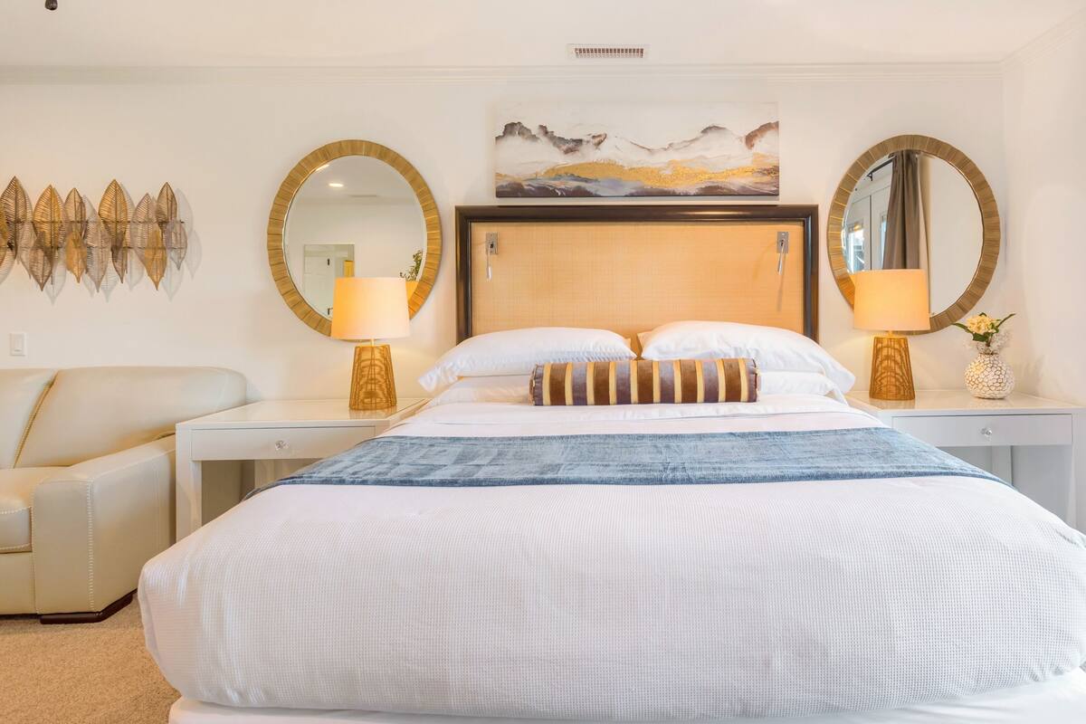 A hotel room with a large bed, two bedside tables with lamps, a sofa, and a painting above the bed.