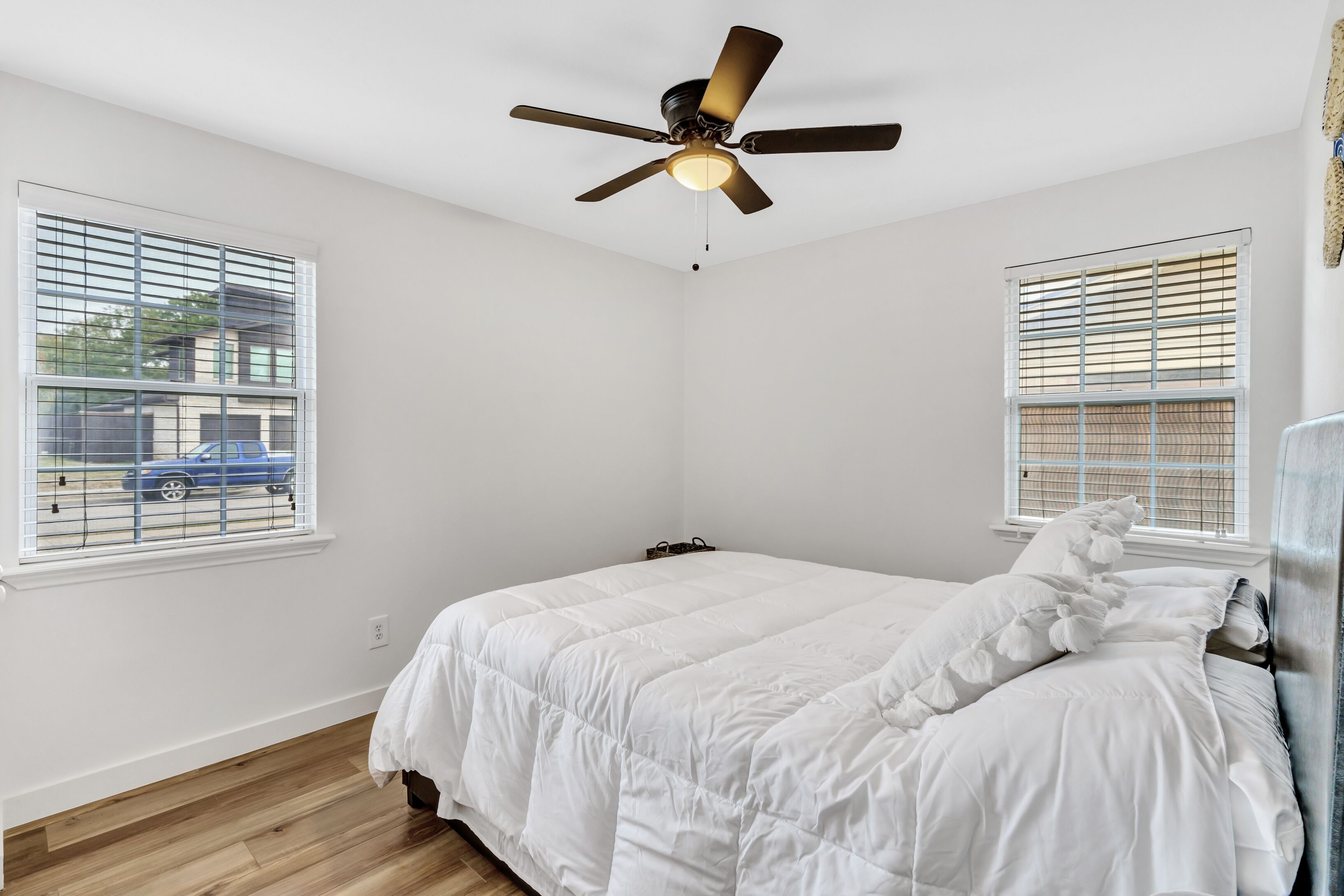 Une chambre à coucher avec un lit, un ventilateur de plafond et deux fenêtres équipées de stores.