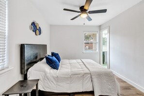 Un dormitorio con una cama, un ventilador de techo, una mesita y una ventana.