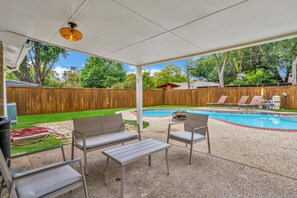 Un patio cubierto con piscina, mobiliario exterior y una cerca de madera.