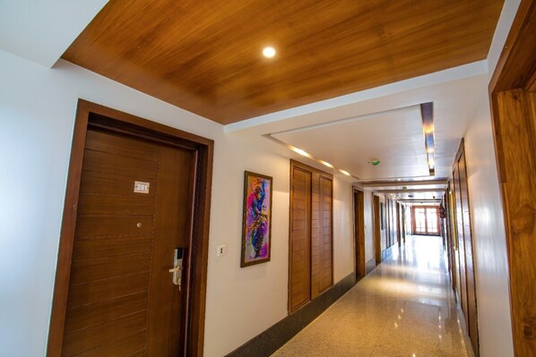 Un pasillo de hotel con puertas de madera, un cuadro en la pared y un largo corredor que lleva a una habitación luminosa.