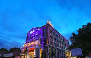Un hôtel avec une enseigne bien visible et une façade illuminée au crépuscule.