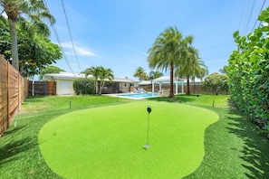 A backyard with a putting green, a pool, and a house in the background. - Heated Pool, Golf & Grill Oasis, Sleeps 6 (Palm Beach Gardens)