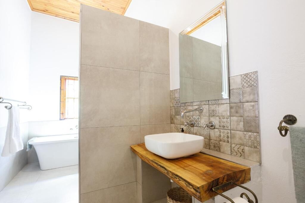 A bathroom with a wooden vanity, a white sink, a bathtub, and patterned tiles.