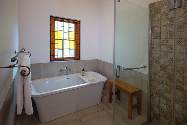 A bathroom with a bathtub, a window, a shower, and a wooden bench. - 06 On Burger (De Rust)