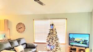 Una sala de estar con un sofá de cuero negro, una mesa de centro, un árbol de Navidad, un televisor y un ventilador de techo.