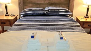 Una cama bien hecha con almohadas a rayas, un adorno de velero en la pared y dos lámparas de noche.