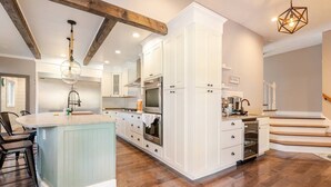 Une cuisine spacieuse avec des meubles blancs, un îlot central et un escalier en bois.