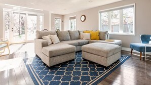 Un salon spacieux avec un canapé d’angle, un pouf et un tapis bleu à motifs.