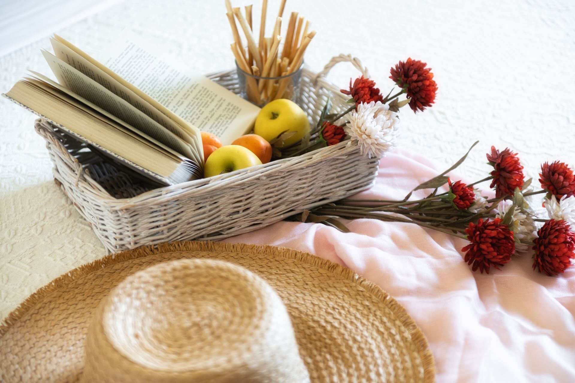 Un panier en osier contenant des livres, des pommes et des fleurs, posé sur une table.