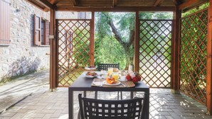 A covered outdoor dining area with a table set for breakfast, surrounded by wooden lattice panels and a stone wall. - Il Gelsomino, apartment between Tuscany and Umbria (Villastrada)