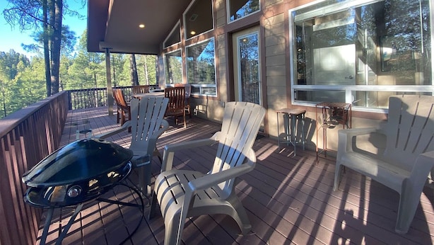 A covered deck with Adirondack chairs and a table, overlooking a forested area. - Home in the Pines • Bathroom for Every Bedroom (Flagstaff)