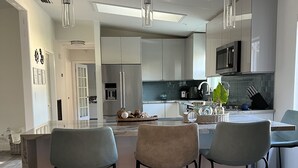 Una cocina moderna con una isla central, taburetes de bar, electrodomésticos de acero inoxidable e iluminación colgante.