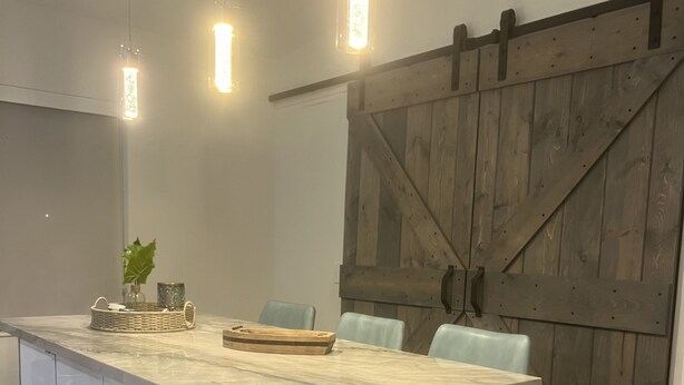 Una cocina moderna con isla de mármol, iluminación colgante y una puerta de madera rústica.