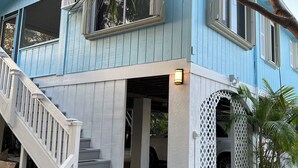 Una casa de dos pisos con fachada azul, una escalera blanca y un porche cubierto.