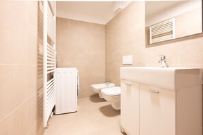 A bathroom with a radiator, a bidet, a toilet, and a sink with a mirror above it.