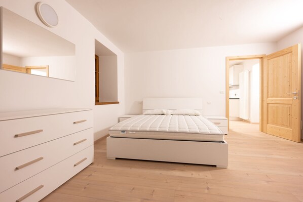 Un dormitorio moderno con una cama, un aparador, un espejo y una puerta de madera.