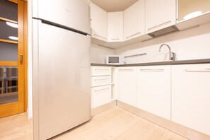 A kitchen with white cabinets, a stainless steel refrigerator, a microwave, and a sink.