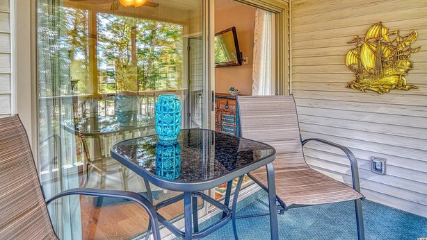 A glass-enclosed porch with a table and chairs, a ceiling fan, and a decorative wall piece.
