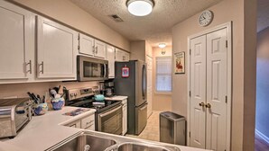 A compact kitchen with white cabinets, stainless steel appliances, a microwave, a refrigerator, and a sink.