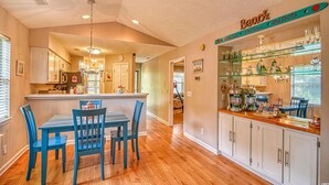 A kitchen with a dining area, wooden flooring, and a bar area with glassware and decorations.