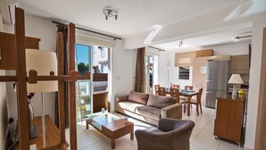 En moderne stue med sofa, sofabord og spiseplads. Der er et køkken med køleskab og skabe.